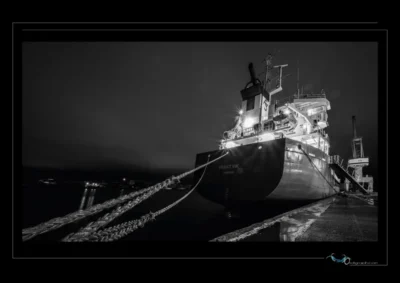 Photo artistique noir et blanc d’un cargo amarré de nuit – ambiance portuaire et infrastructures maritimes. Explorez la puissance visuelle d’un navire industriel dans un port breton, entre reflets, cordages et lumière artificielle. Idéal pour illustrer les métiers de la mer, la logistique nocturne et l’esthétique industrielle. Ordigraph