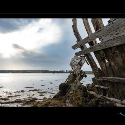 Photo artistique d’une bordée de navire inclinée vers hélice, bois dégradé, lumière douce, ambiance portuaire abandonnée. Idéal pour blog sur patrimoine maritime, design nostalgique ou inspiration artistique. Mots-clés : bordée navire, hélice marine, bois penché, épave bateau, photographie artistique, textures maritimes, Ordigraph