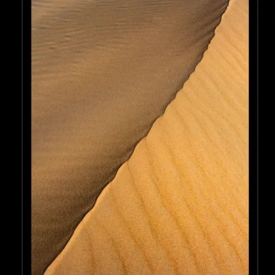 Photographie artistique de dunes contrastées – image de désert avec textures naturelles, sable sombre et clair, composition minimaliste, paysage désertique, art visuel inspiré par la nature, photo de dunes pour décoration murale, photographie fine art du désert, Ordigraph.