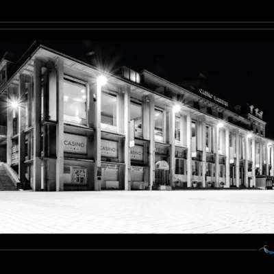 Photo en noir et blanc du Casino Barrière de Dinard vue depuis la digue. Architecture classique illuminée dans la nuit, ambiance élégante et mystérieuse. Composition artistique mettant en valeur le patrimoine urbain et côtier breton, idéale pour illustrer Dinard la nuit. Ordigraph