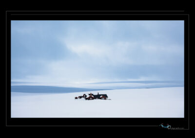 Photo hivernale en Laponie avec habitations isolées dans un paysage enneigé, collines douces, ciel nuageux et ambiance minimaliste. Image scandinave haute définition, nature arctique, solitude nordique, atmosphère calme et contemplative. Idéal pour blog de voyage, site photo, inspiration nordique et récits visuels. Ordigraph