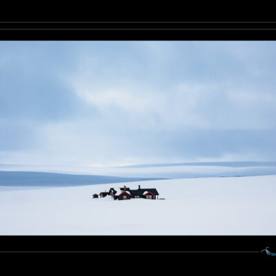 Photo hivernale en Laponie avec habitations isolées dans un paysage enneigé, collines douces, ciel nuageux et ambiance minimaliste. Image scandinave haute définition, nature arctique, solitude nordique, atmosphère calme et contemplative. Idéal pour blog de voyage, site photo, inspiration nordique et récits visuels. Ordigraph