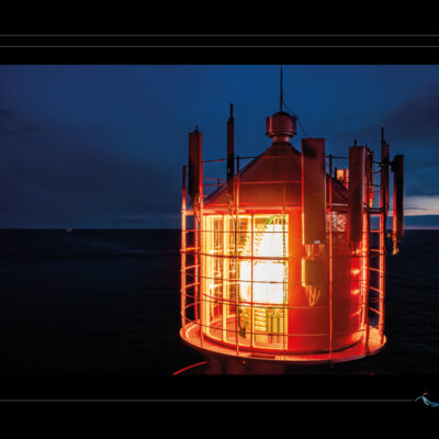 Photo nocturne du phare de Lindesnes en Norvège, vue rapprochée de la lanterne illuminée, ciel sombre, mer calme et ambiance maritime. Image scandinave haute définition, architecture emblématique, lumière de veille et atmosphère contemplative. Idéal pour blog de voyage, site photo, inspiration nordique et récits visuels. Ordigraph